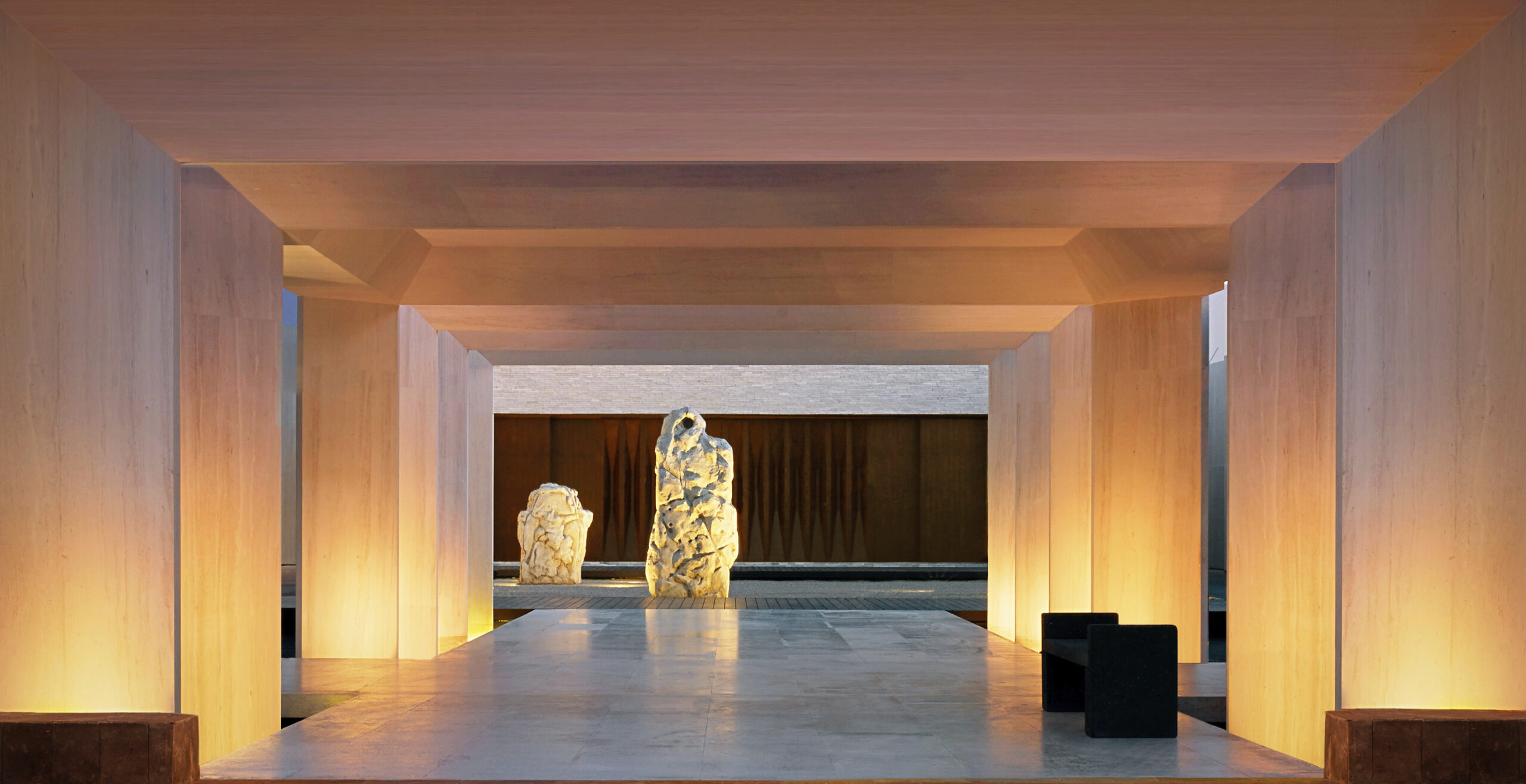 stone arches leading to stone sculptures and the entrance of nobu hotel los cabos. dramatic nightime lighting.
