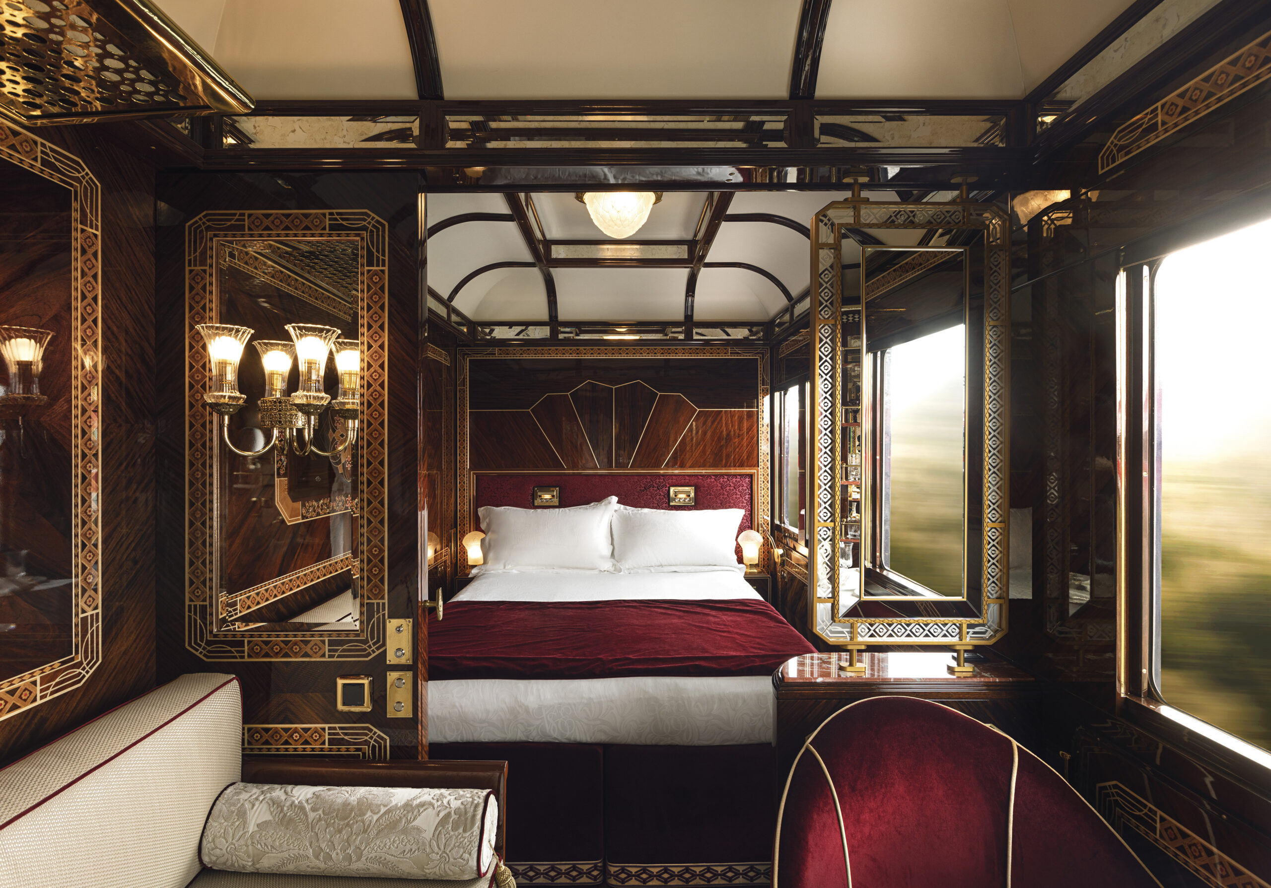 grand suite at the venice simplon orient express with inlaid wood paneling, red velvet upholstery and classic elegant glass lalique wall lights