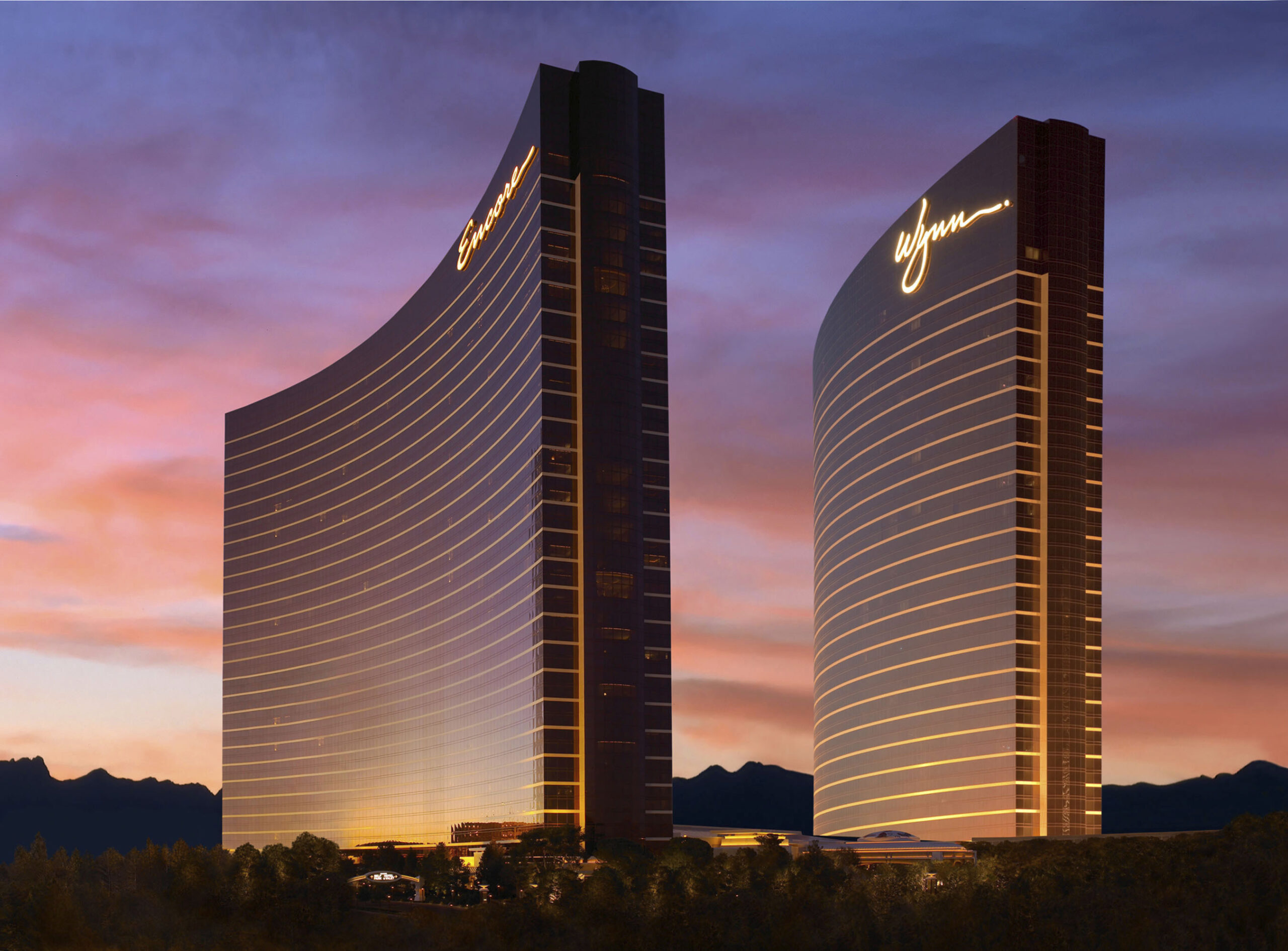 Wynn and Encore Las Vegas curved hotel towers illuminated at sunset, with golden balcony lighting against a pink and purple sky.
