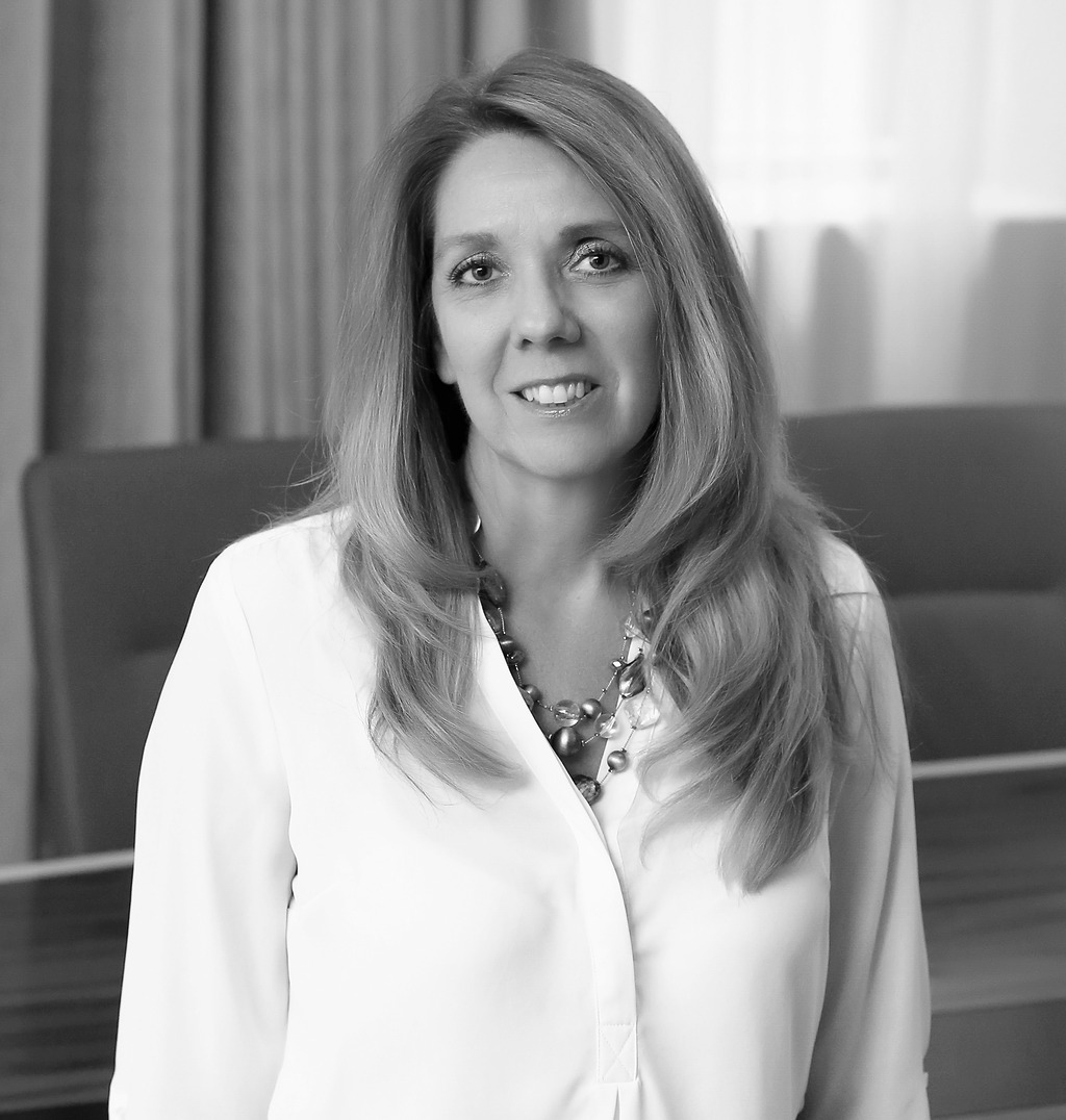 Black and white portrait of Susan Bruce, Wimberly Interiors, smiling against a grey backdrop.