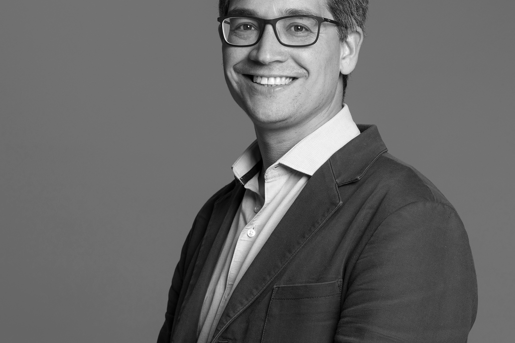Black and white portrait of Tony Menezes, WATG, smiling against a grey backdrop.