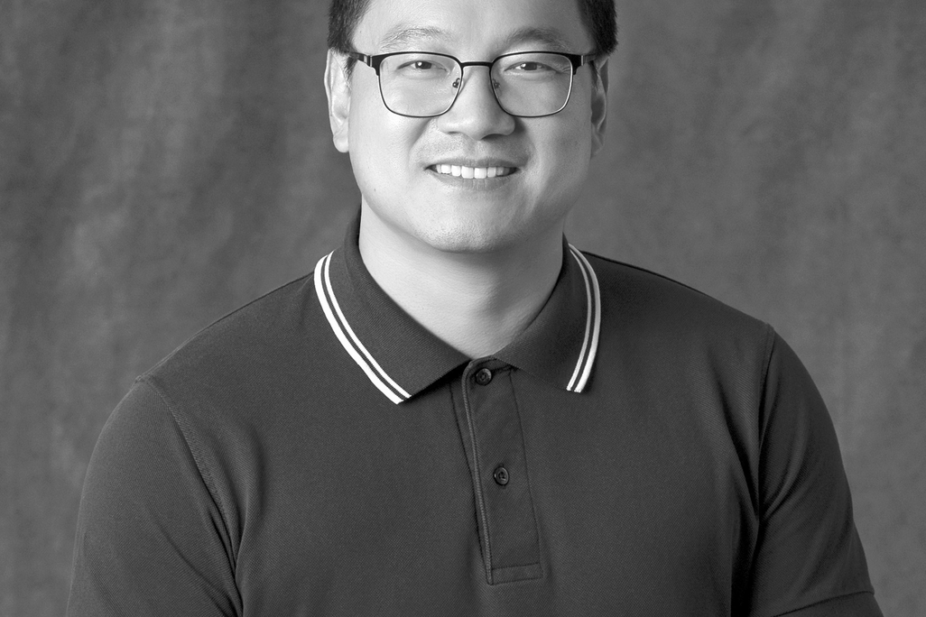 Black and white portrait of Xin Li, WATG, smiling against a grey backdrop.