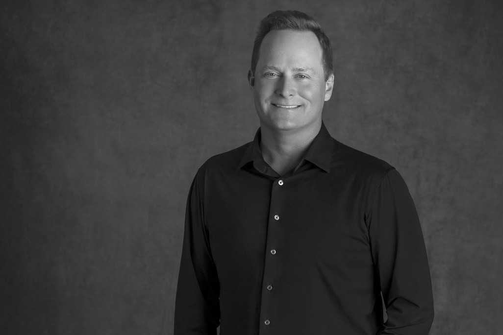 Black and white portrait of Lance Walker, WATG, smiling against a grey backdrop.