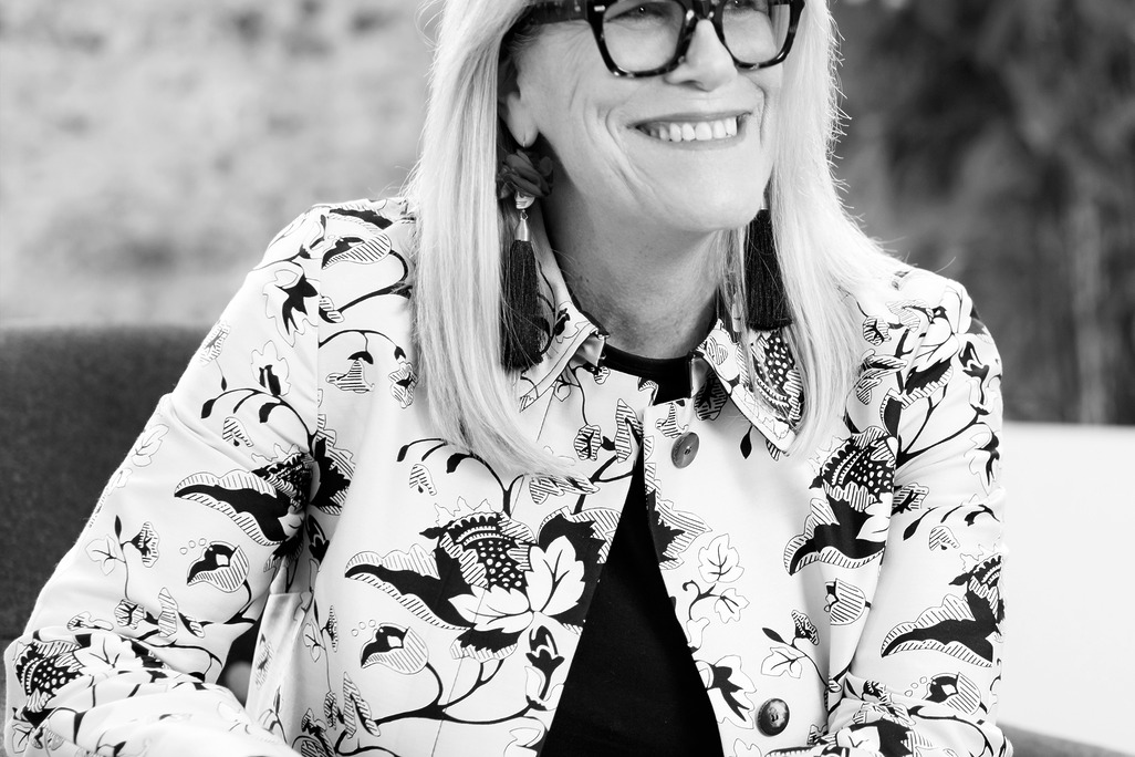 Black and white portrait of Margaret McMahon, Wimberly Interiors, smiling against a grey backdrop.