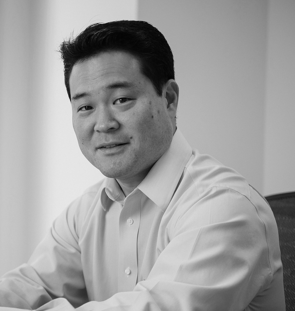 Black and white portrait of Mark Yoshizaki, WATG, smiling against a grey backdrop.