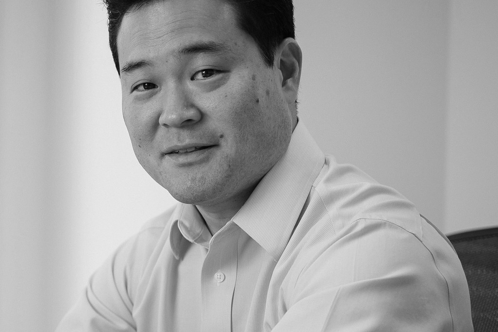 Black and white portrait of Mark Yoshizaki, WATG, smiling against a grey backdrop.
