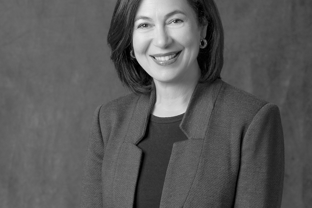 Black and white portrait of Monica Cuervo, WATG, smiling against a grey backdrop.