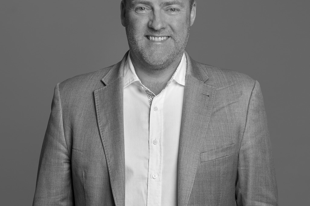 Black and white portrait of Nick Carrier, WATG, smiling against a grey backdrop.