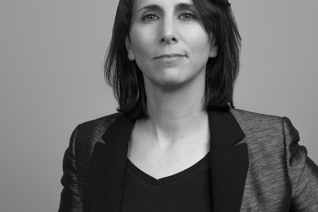 Black and white portrait of Nicole Hammond, WATG, smiling against a grey backdrop.