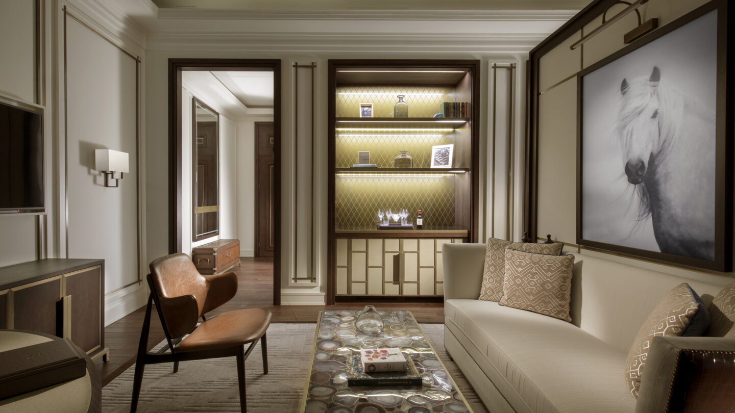 st regis astana suite sitting room in neutral colours with quartz table, leather chair, gold bookcase and a dramatic painting of a white horse