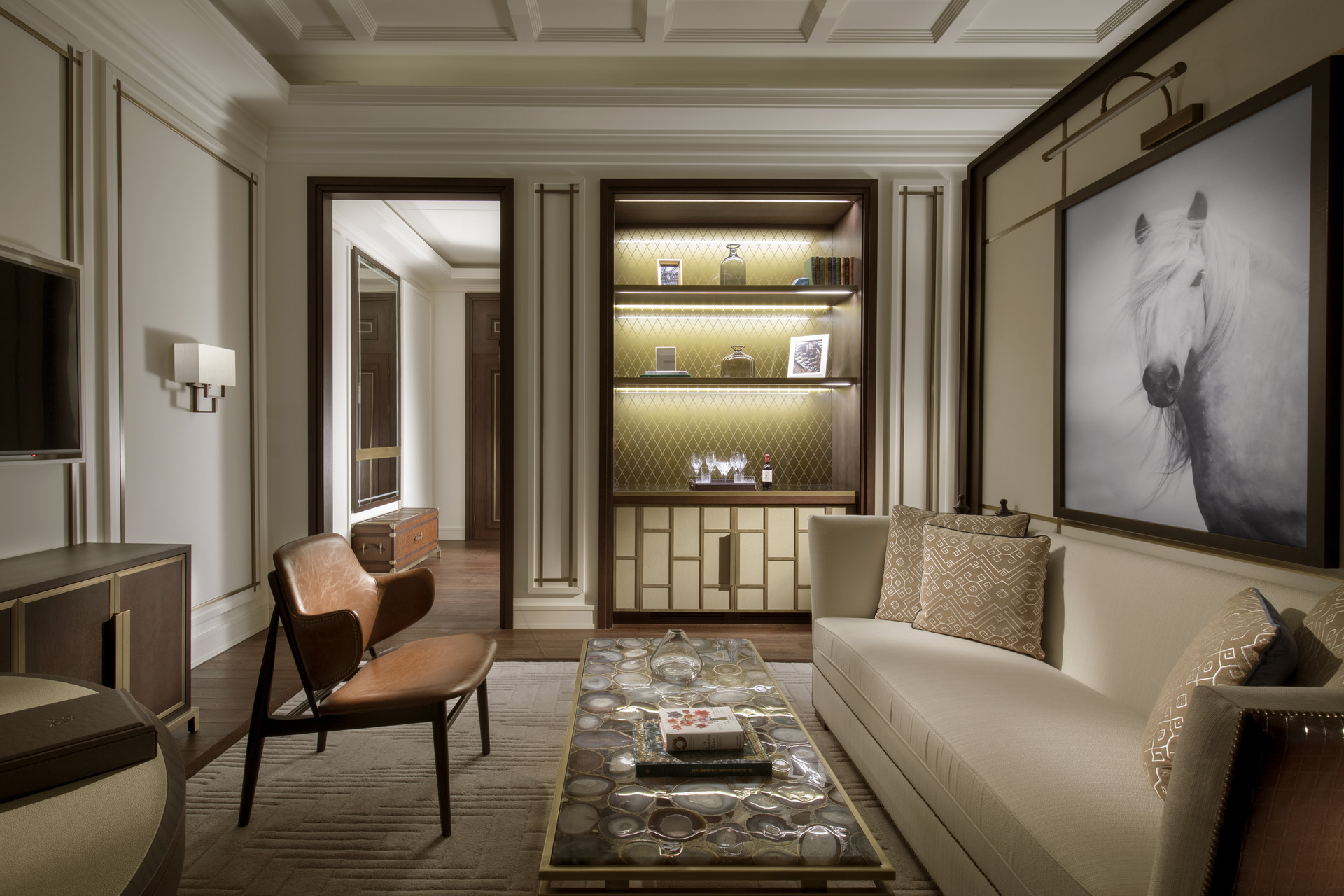 st regis astana suite sitting room in neutral colours with quartz table, leather chair, gold bookcase and a dramatic painting of a white horse