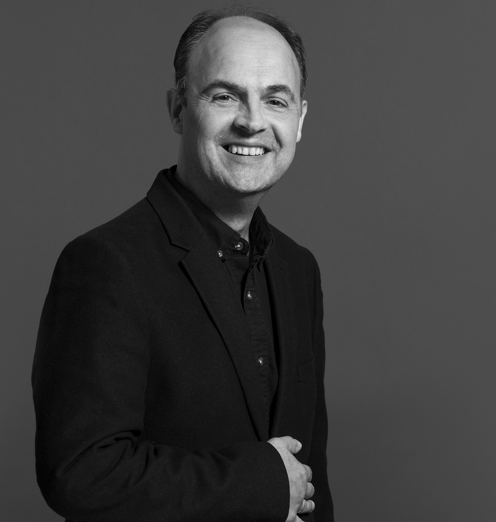 Black and white portrait of Alain De Villoutreys, WATG, smiling against a grey backdrop.