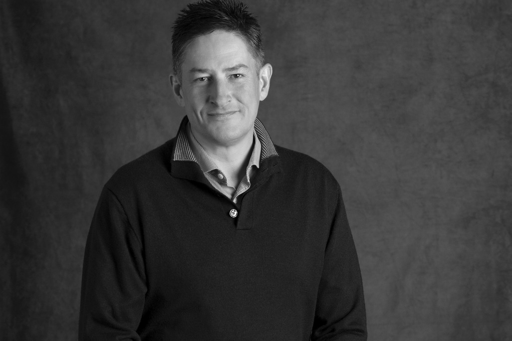 Black and white portrait of Ashley Scott, WATG, smiling against a grey backdrop.