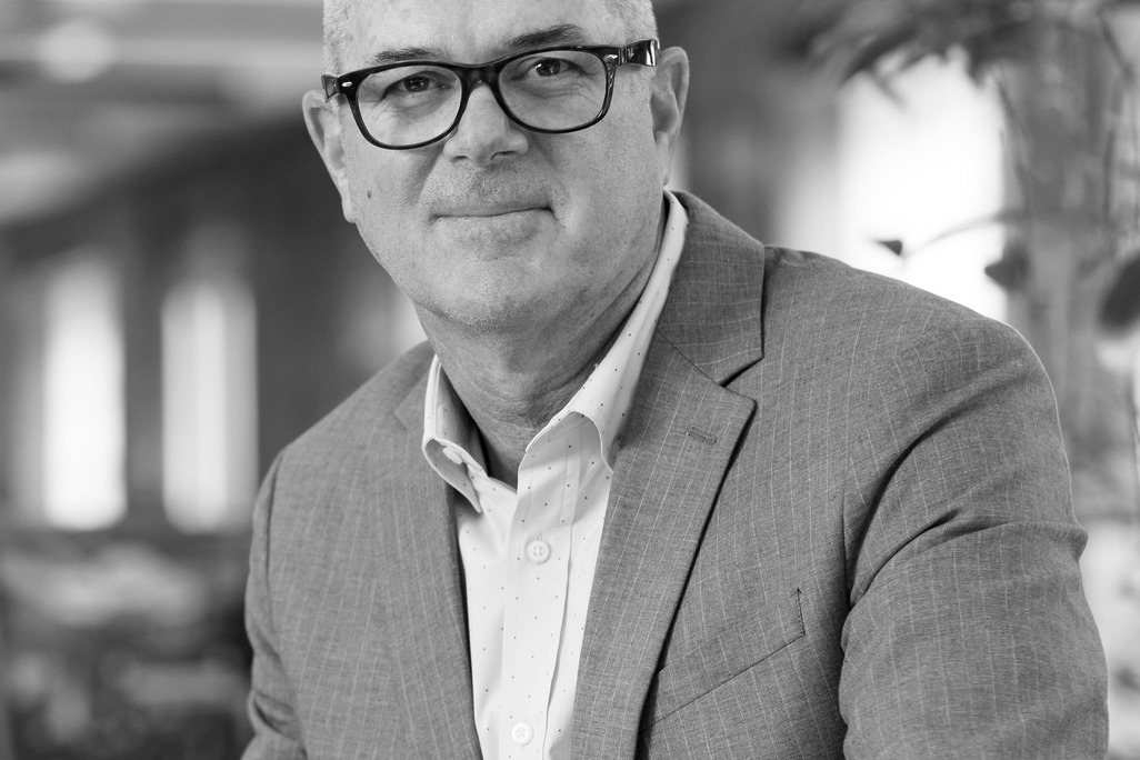 Black and white portrait of Bryan Algeo, WATG, smiling against a grey backdrop.