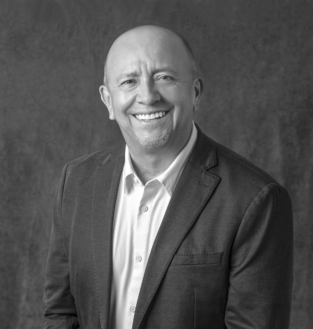Black and white portrait of Greg Villegas, WATG, smiling against a grey backdrop.