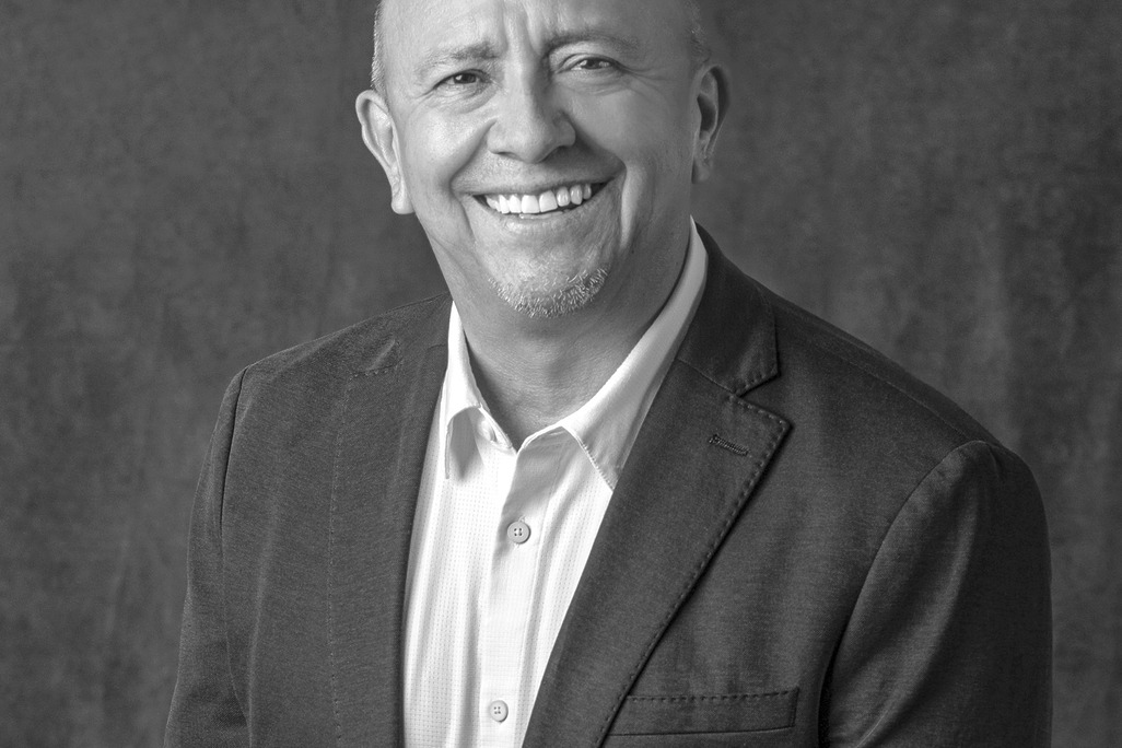 Black and white portrait of Greg Villegas, WATG, smiling against a grey backdrop.
