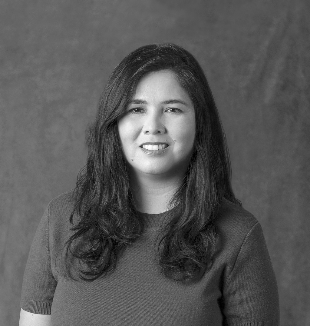 Black and white portrait of Natalie Ruiz, WATG, smiling against a grey backdrop.