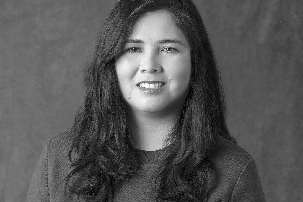 Black and white portrait of Natalie Ruiz, WATG, smiling against a grey backdrop.