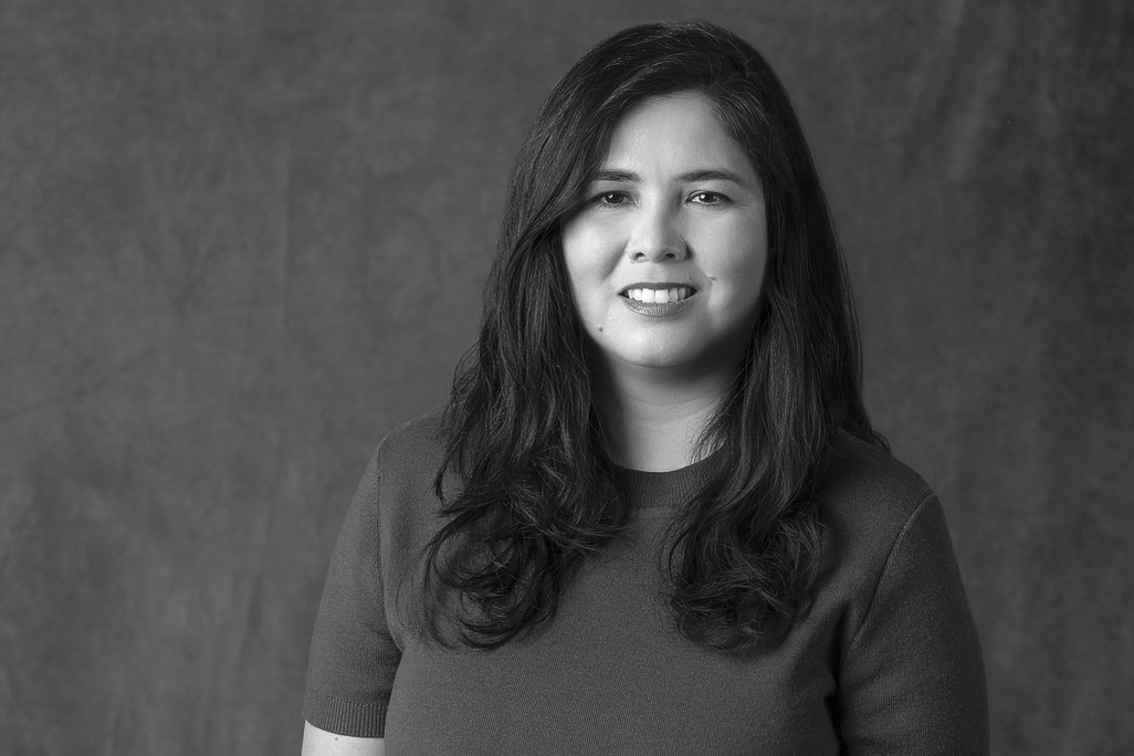 Black and white portrait of Natalie Ruiz, WATG, smiling against a grey backdrop.