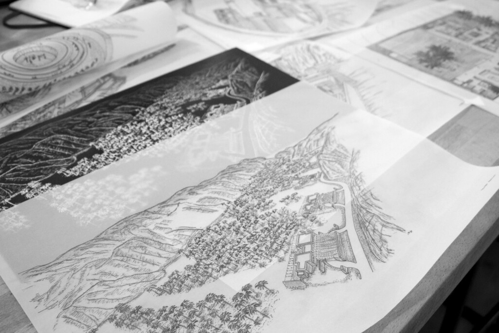 Architectural site drawings and masterplan sketches spread across desk showing landscape and resort design concepts
