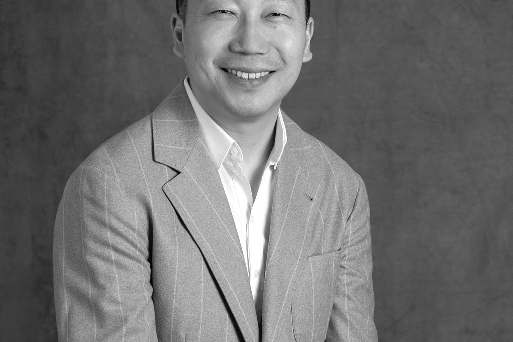 Black and white portrait of Liu Haoyang, Senior Director, Client Services, WATG, smiling against a grey backdrop.
