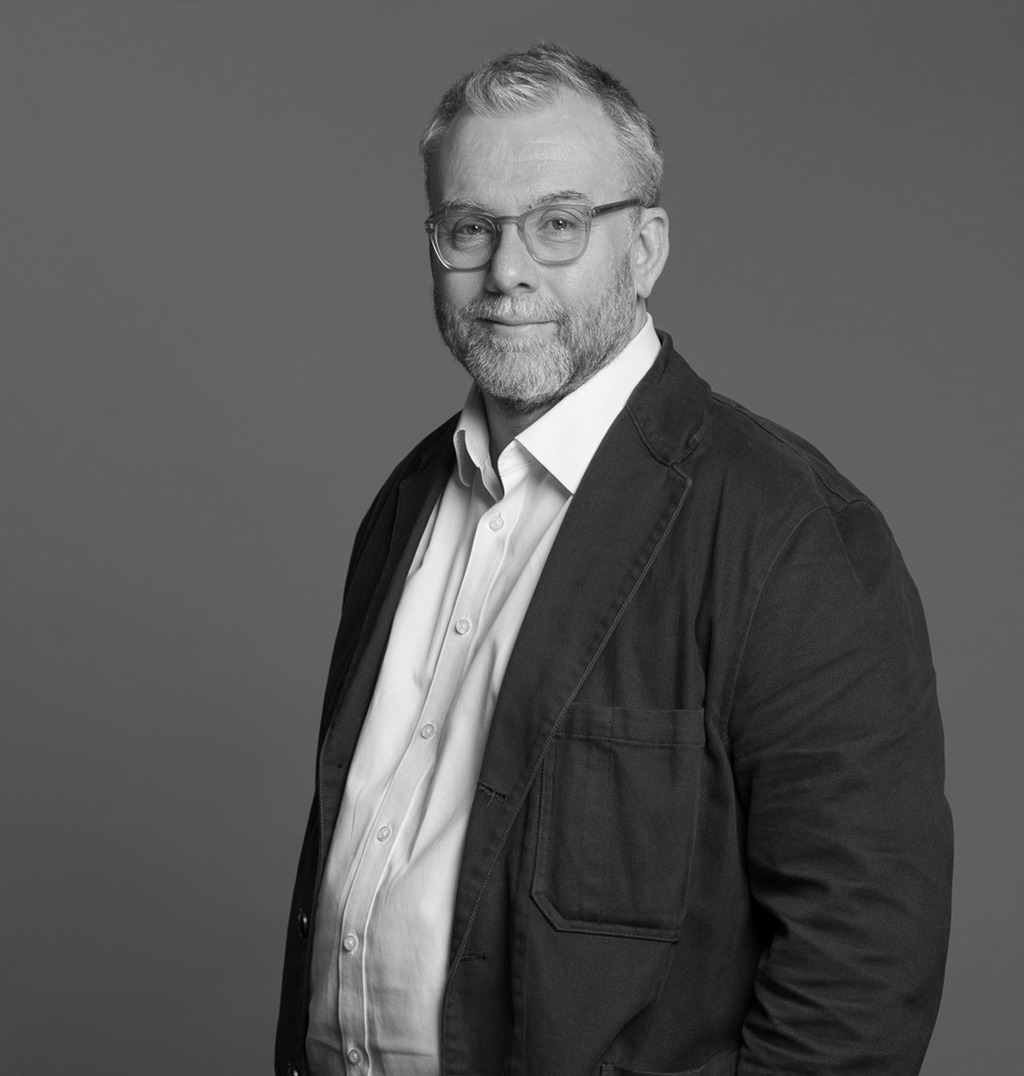 Black and white portrait of Ian Memmott, WATG, smiling against a grey backdrop.