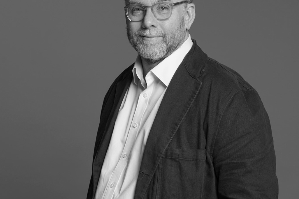 Black and white portrait of Ian Memmott, WATG, smiling against a grey backdrop.
