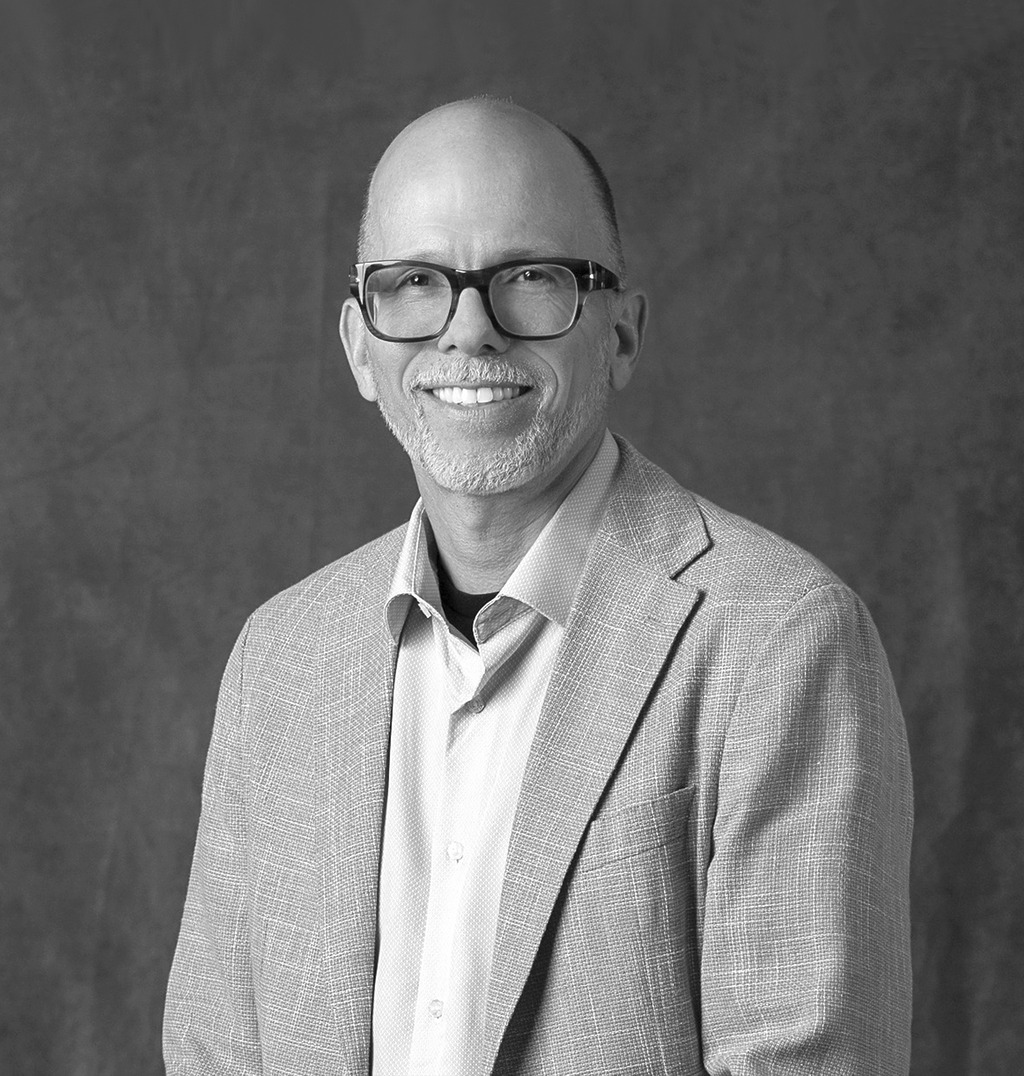 Black and White portrait of Eric Carbonnier, WATG, smiling against a grey backdrop.