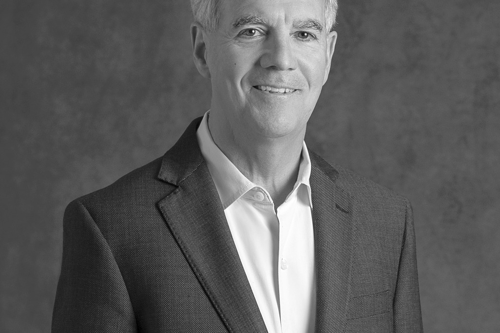 Black and white portrait of Thomas Sykes, WATG, smiling against a grey backdrop.
