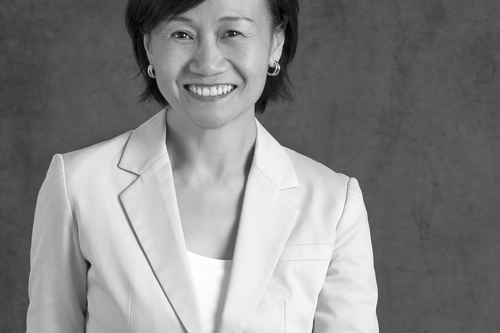 Black and white portrait of Christine Chung, WATG, smiling against a grey backdrop.
