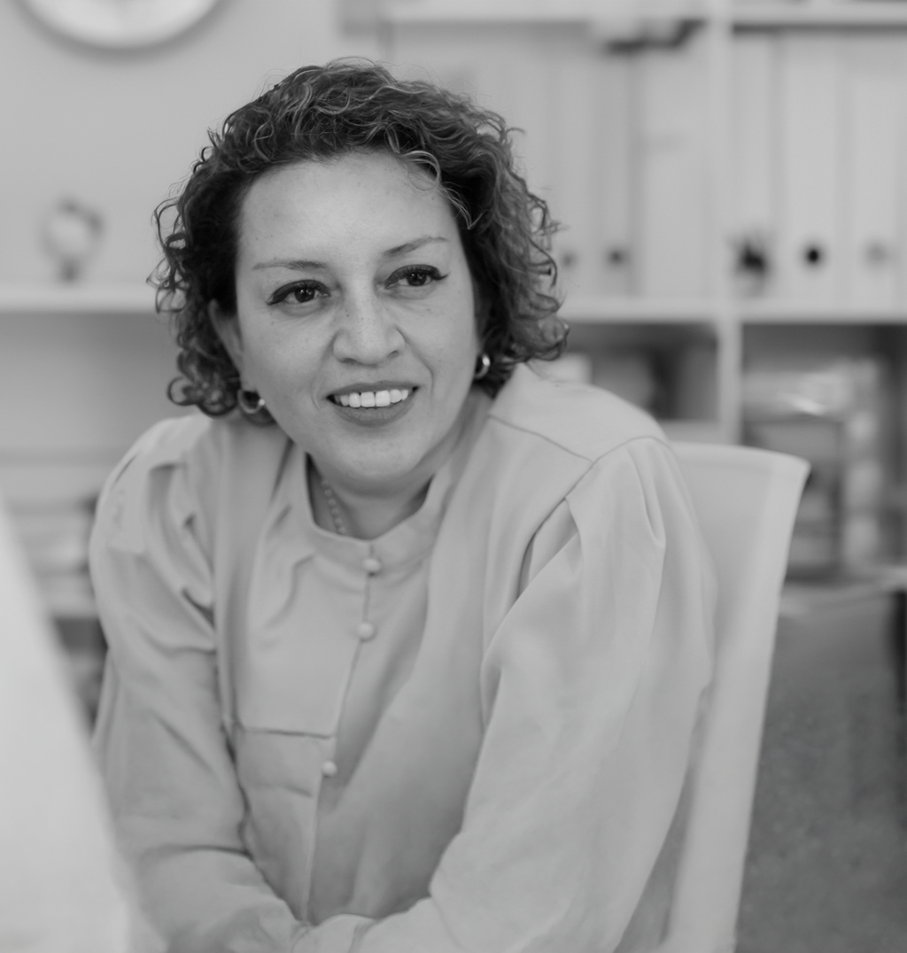 Black and white portrait of Margarita Velez-Mantovani, Wimberly Interiors, smiling against a grey backdrop.