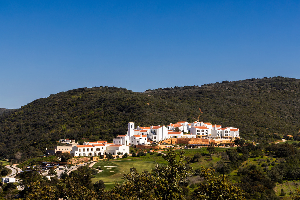 Viceroy at Ombria Algarve, a cluster of whitewashed buildings with terracotta roofs and a bell tower, set on a wooded hillside above a golf course.