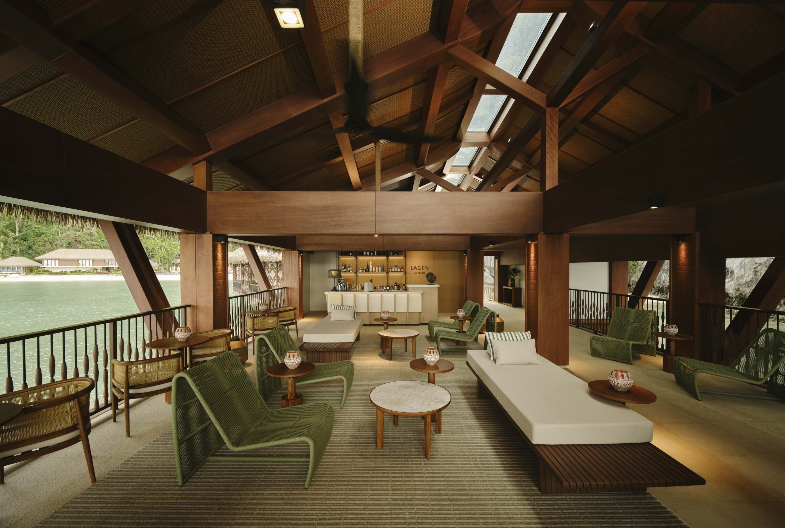 The Boathouse lounge at Lagen El Nido, a tranquil overwater space defined by deep timber tones, woven green lounge chairs, and a direct connection to the bay.