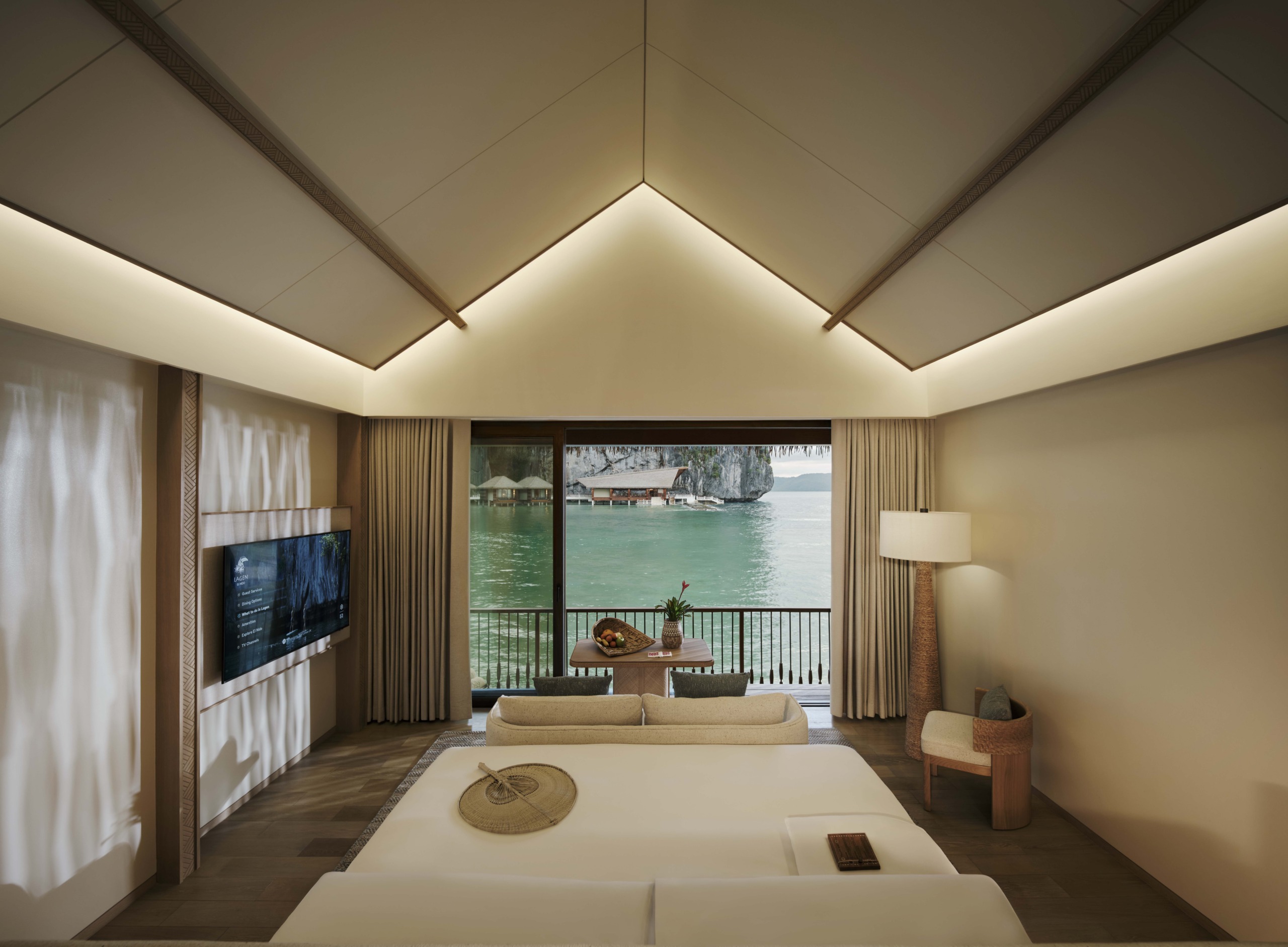 The interior of a Water Villa showcasing a vaulted ceiling and a minimalist design language, framing an unobstructed view of the turquoise bay and limestone cliffs.