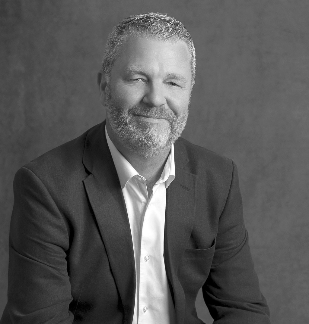 Black and white portrait of Sean Roche, WATG, smiling against a grey backdrop.