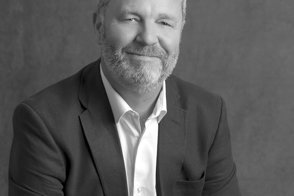 Black and white portrait of Sean Roche, WATG, smiling against a grey backdrop.