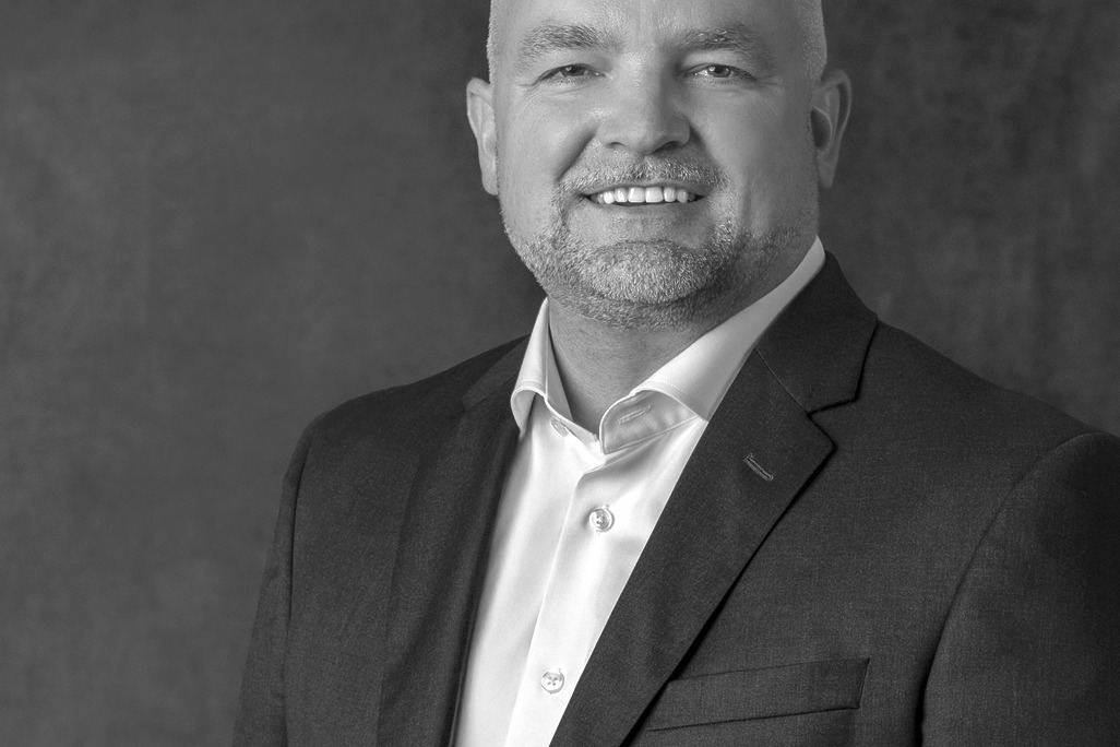 Black and white portrait of Dan Patton, WATG, smiling against a grey backdrop.