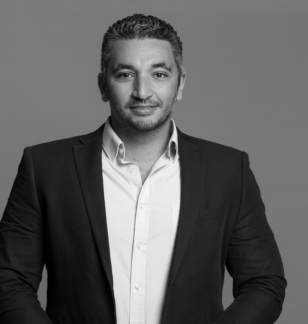 Black and white portrait of Ahmed Ibrahim, WATG, smiling against a grey backdrop.