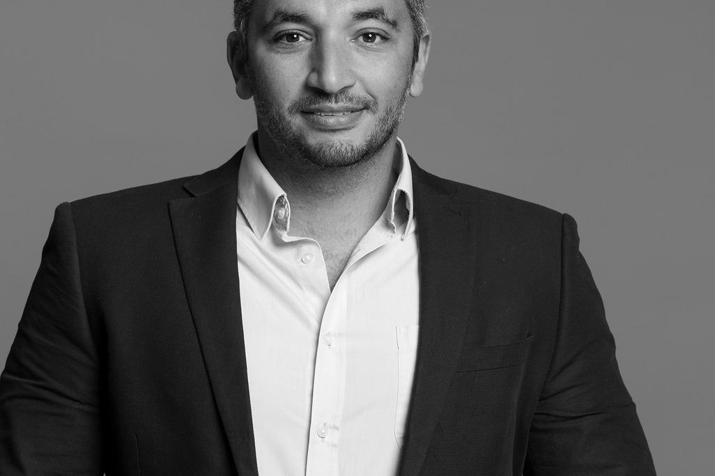 Black and white portrait of Ahmed Ibrahim, WATG, smiling against a grey backdrop.