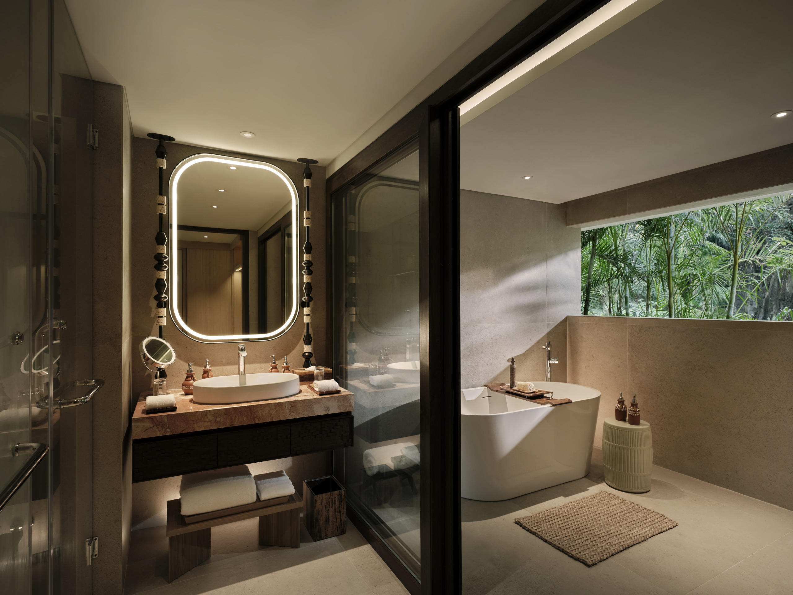 Lagen Island Resort El Nido bathroom with a vessel sink, backlit rounded mirror, freestanding oval tub, and a jungle garden view through a clerestory window.