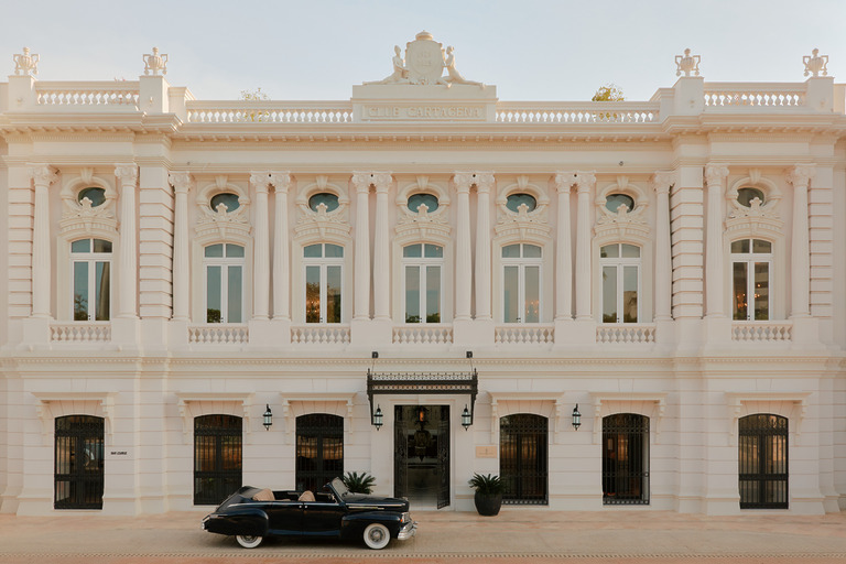 Four Seasons Hotel Cartagena facade, cream neoclassical building with ornate detailing and a vintage black convertible parked at the entrance.