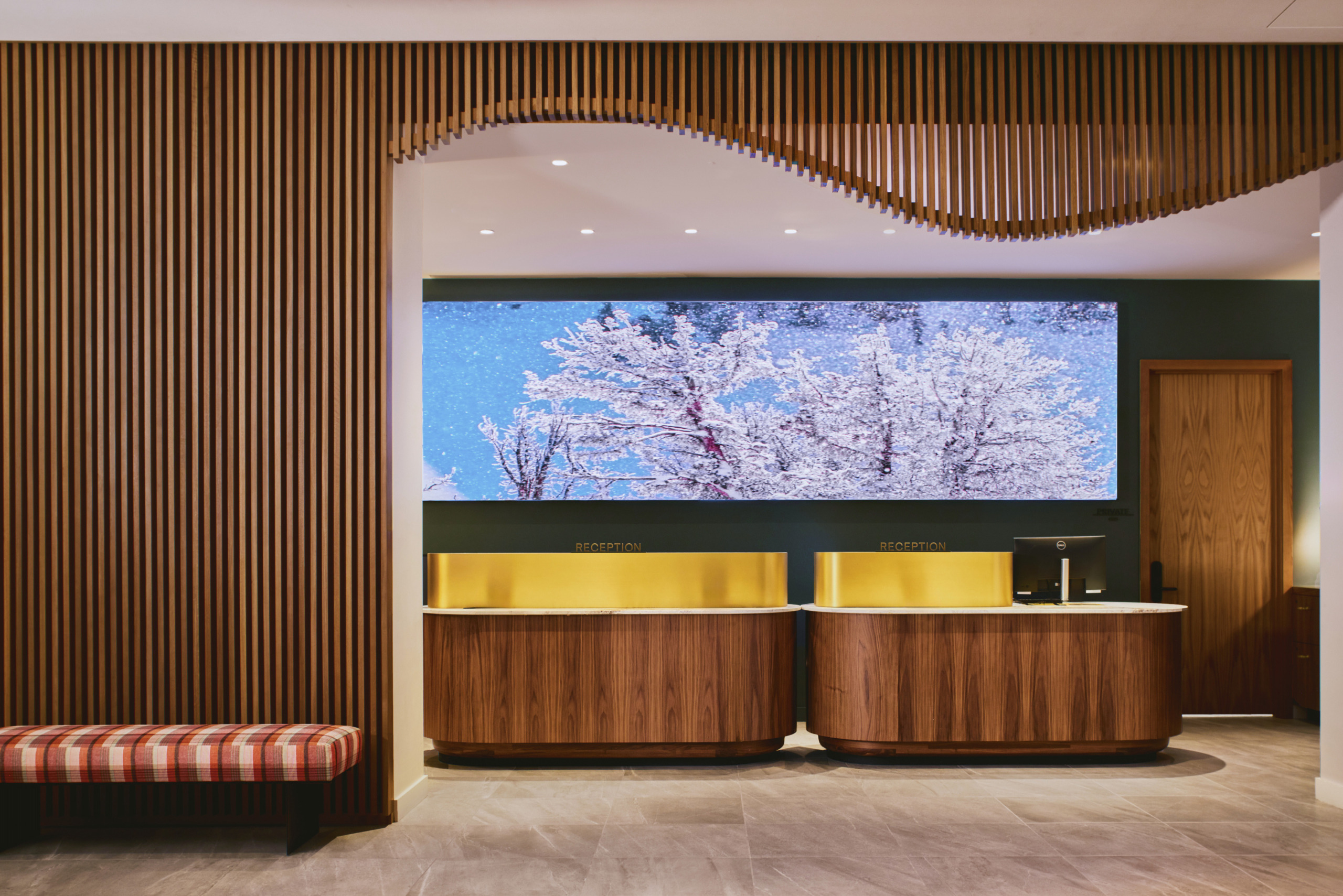 Reception desk with warm timber panelling, slatted wood feature wall, and large backlit floral display at Limelight Hotel Mammoth Lakes, designed by WATG