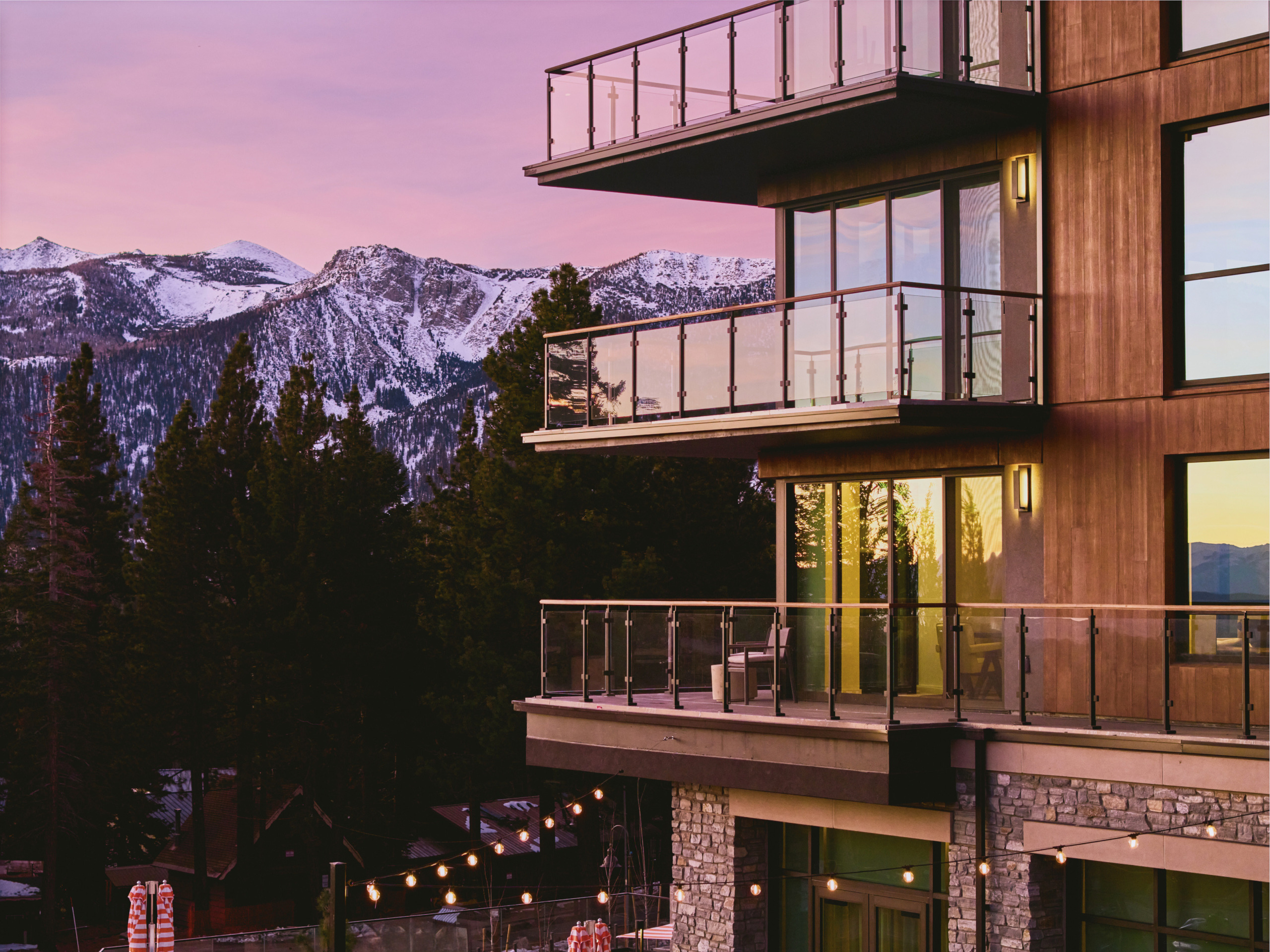 Dusk exterior of Limelight Hotel Mammoth Lakes residences with illuminated balconies and pine-forested mountain range in the background, designed by WATG