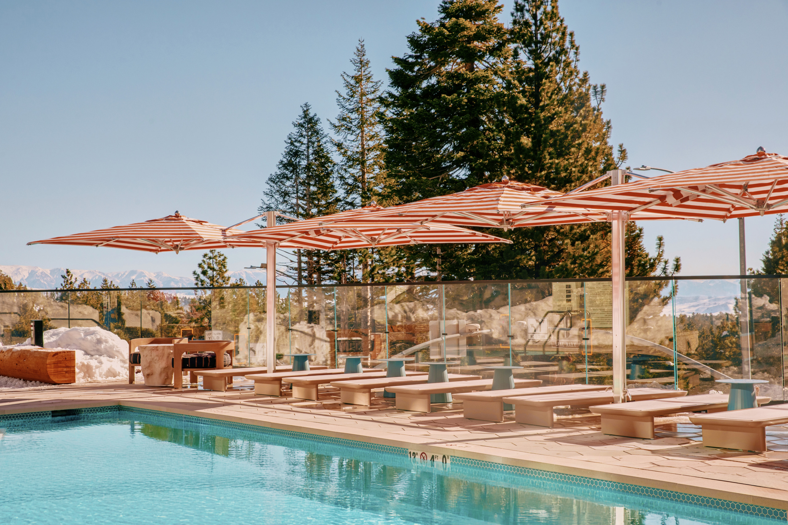 Outdoor pool terrace with sun loungers, parasols, and pine tree views at Limelight Hotel Mammoth Lakes, designed by WATG