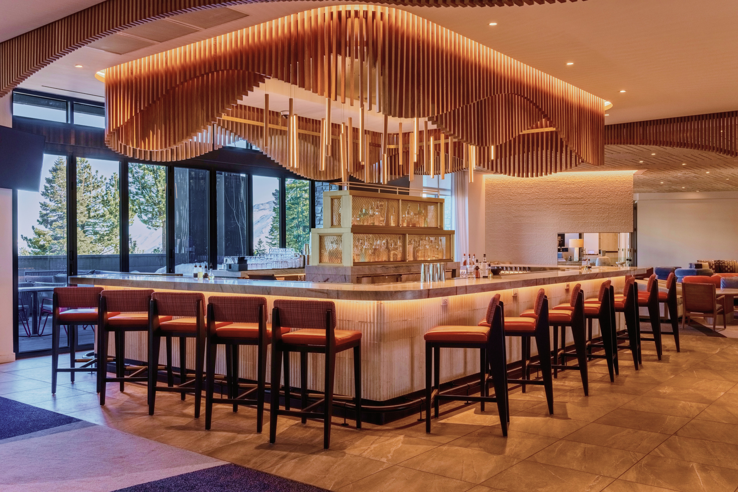 Hotel bar with sculptural copper pendant ceiling feature, timber bar counter, and floor-to-ceiling glazing at Limelight Hotel Mammoth Lakes, designed by WATG