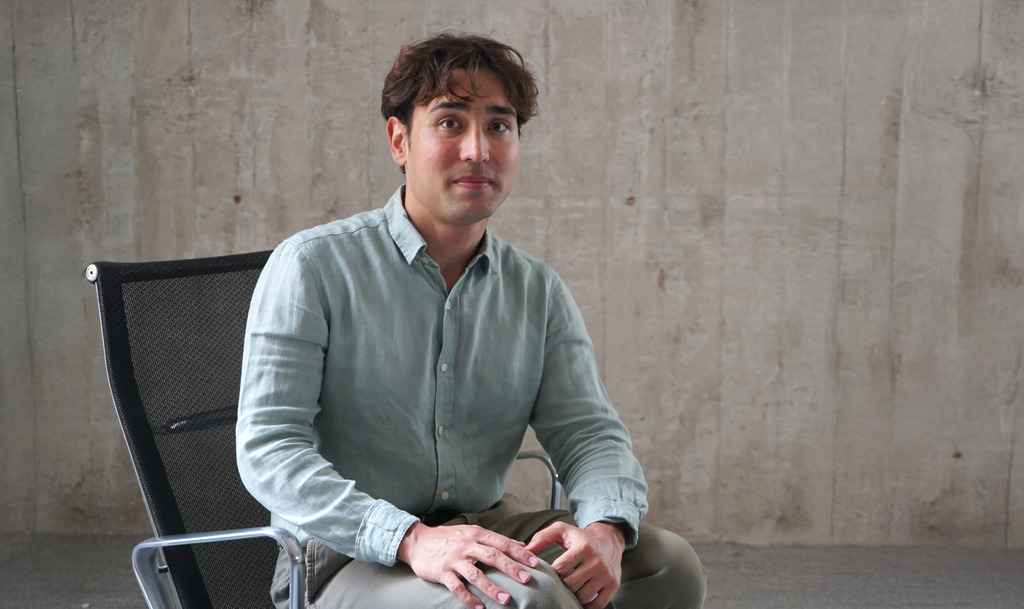 Ethan Ilktan, Architectural Designer at WATG's Los Angeles office, seated in a chair against a concrete wall.