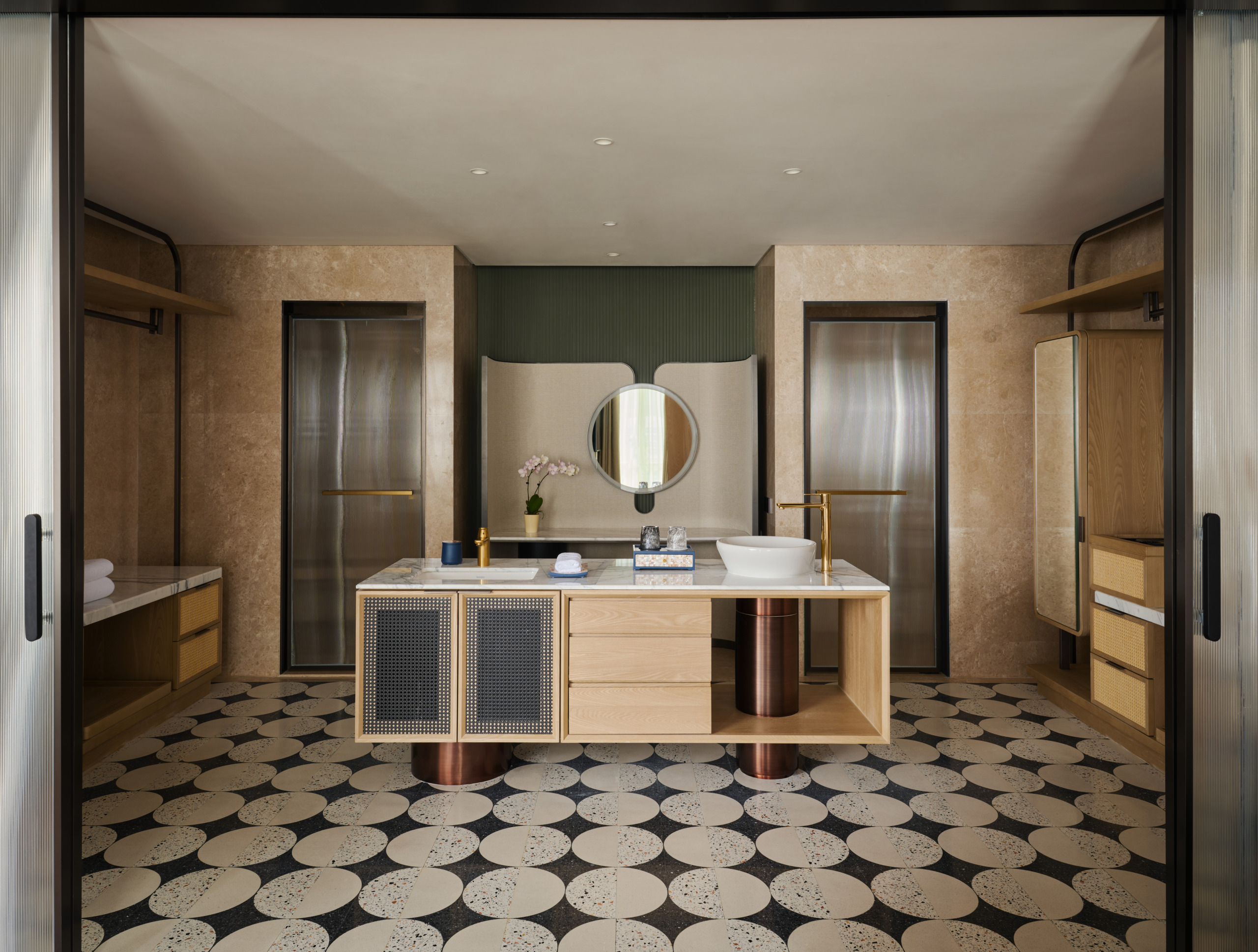 Hotel Indigo Zhuhai suite bathroom with floating oak vanity, brass fittings, round mirror, and bold terrazzo circle-pattern floor tiles.