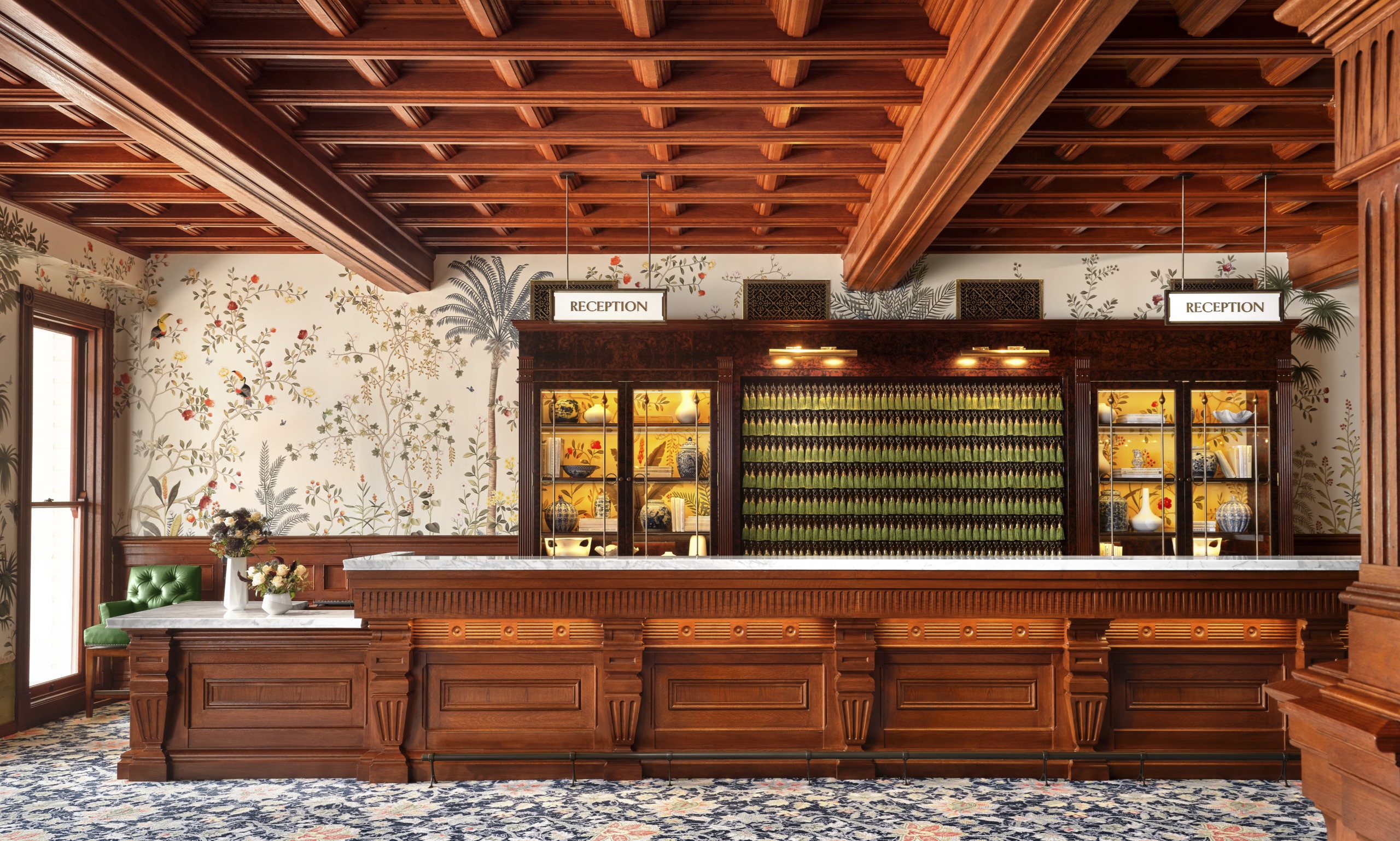 Hotel del Coronado reception desk with ornate carved wood panelling, coffered ceiling, botanical wallpaper, and floral carpet.