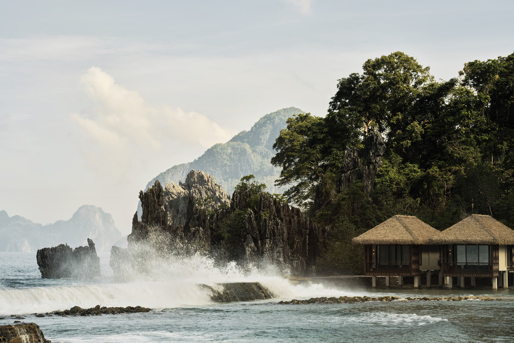 Overwater villas at Lagen Island Resort, El Nido, set against limestone cliffs as waves crash on the shore