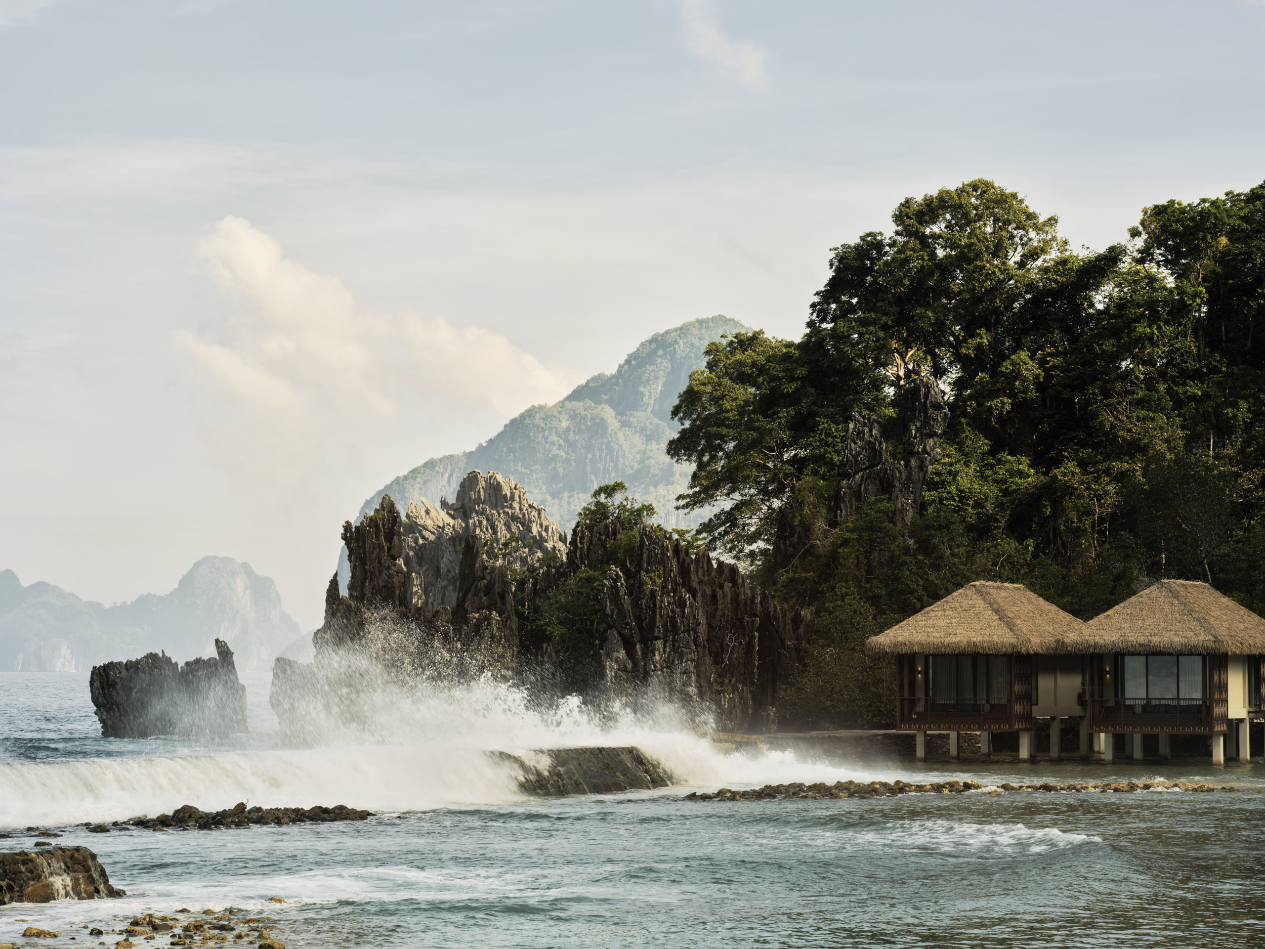 Overwater villas at Lagen Island Resort, El Nido, set against limestone cliffs as waves crash on the shore